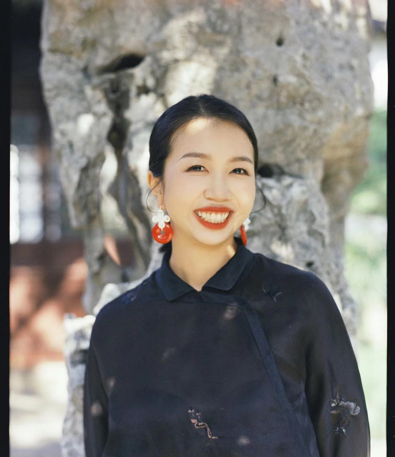 Woman in black shirt wearing red earrings standing in front of a tree