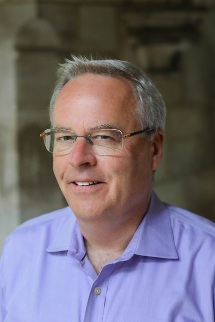 Man in blue shirt with glasses in front of a stone building