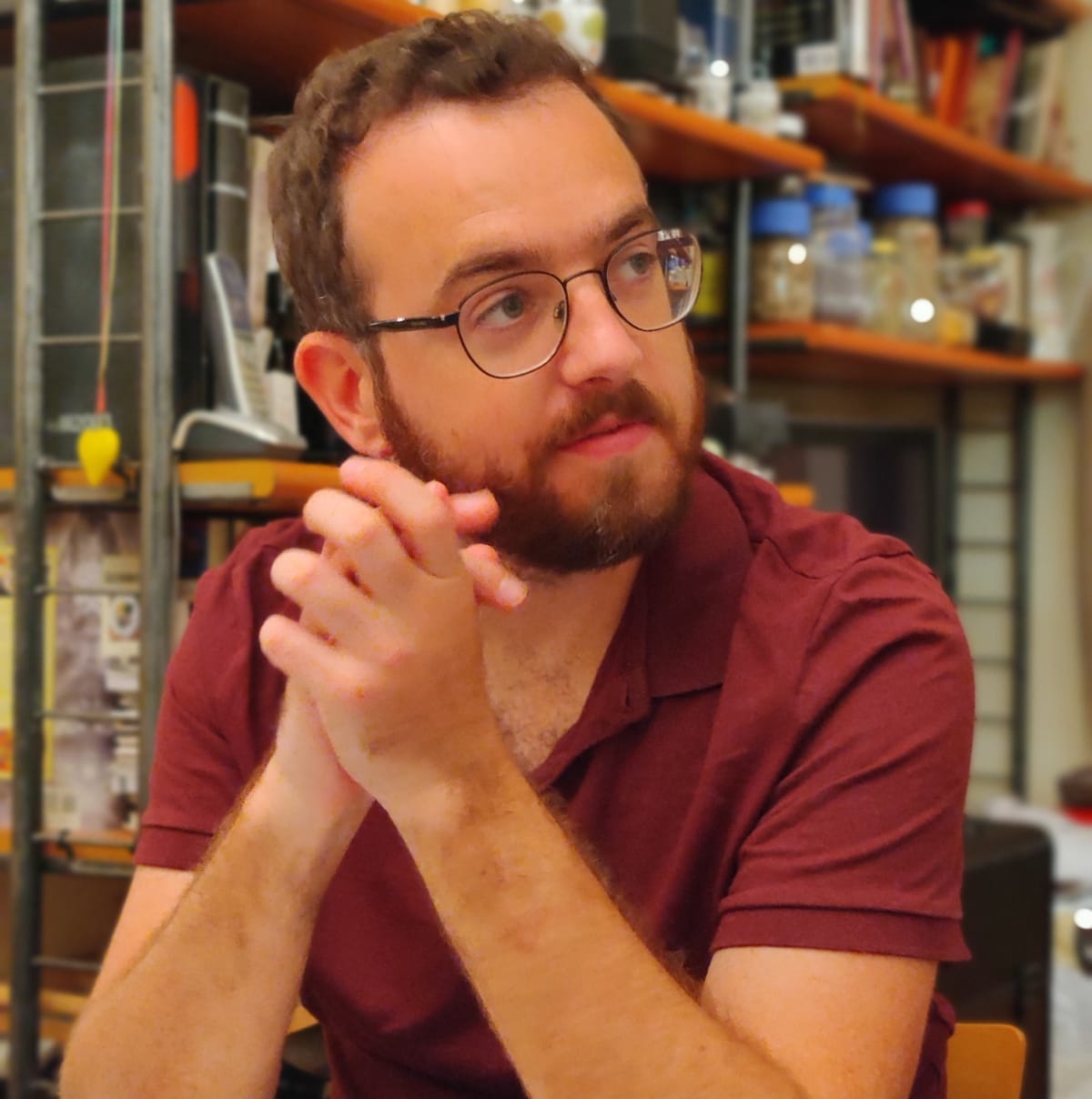 man in red shirt and glasses in front of a bookshelf