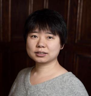 woman with short hair in a grey sweater in front of a dark wood wall